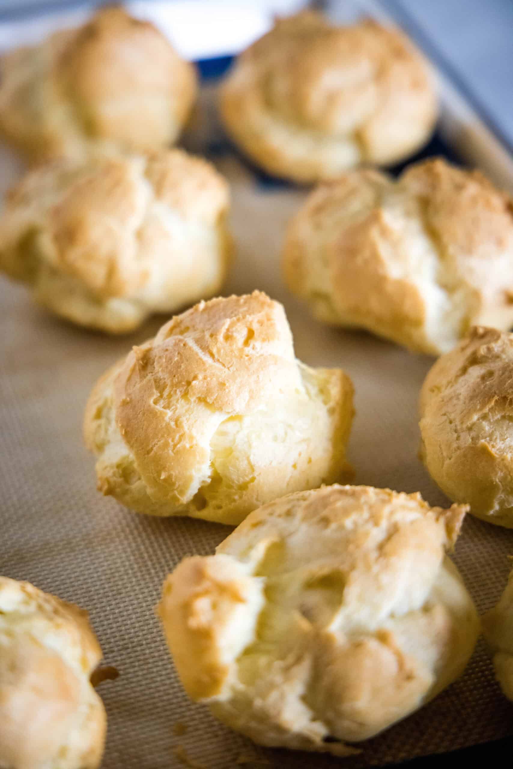 Baked cream puffs on a lined baking sheet.