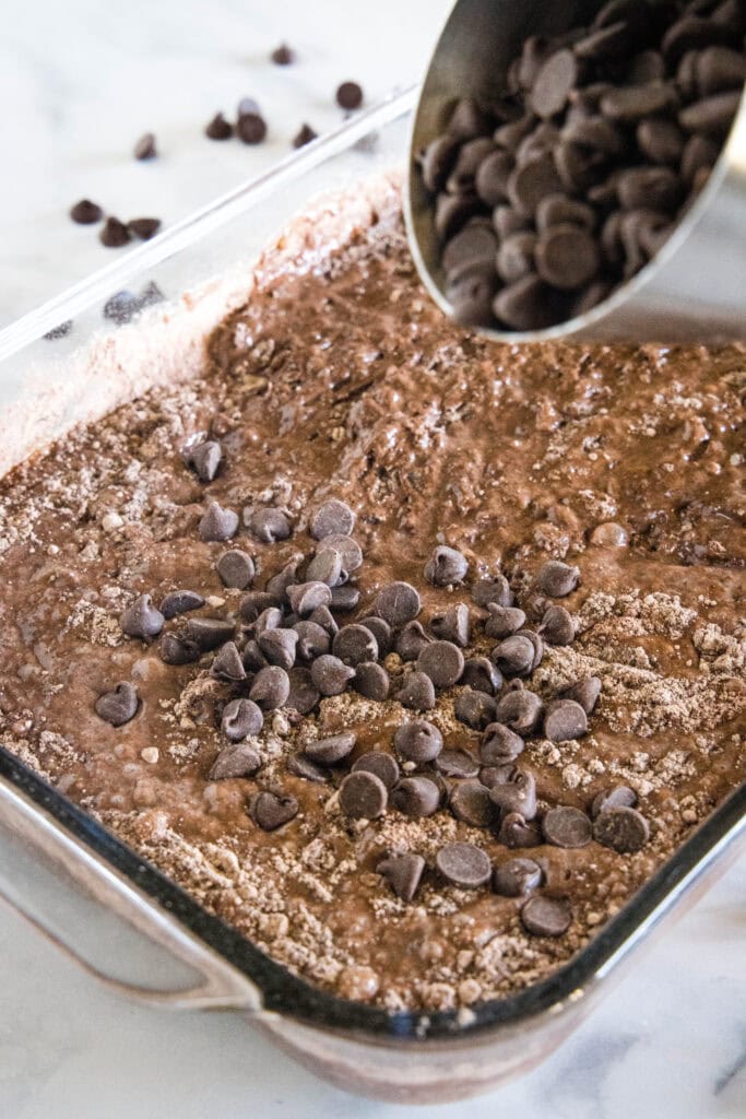Chocolate chips are sprinkled over top of chocolate dump cake ingredients in a glass baking dish.