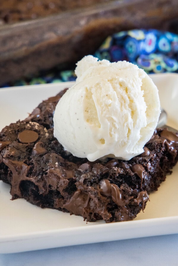 A slice of chocolate dump cake topped with a scoop of vanilla ice cream on a white plate.