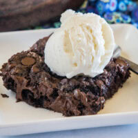 A slice of chocolate dump cake topped with a scoop of vanilla ice cream on a white plate.