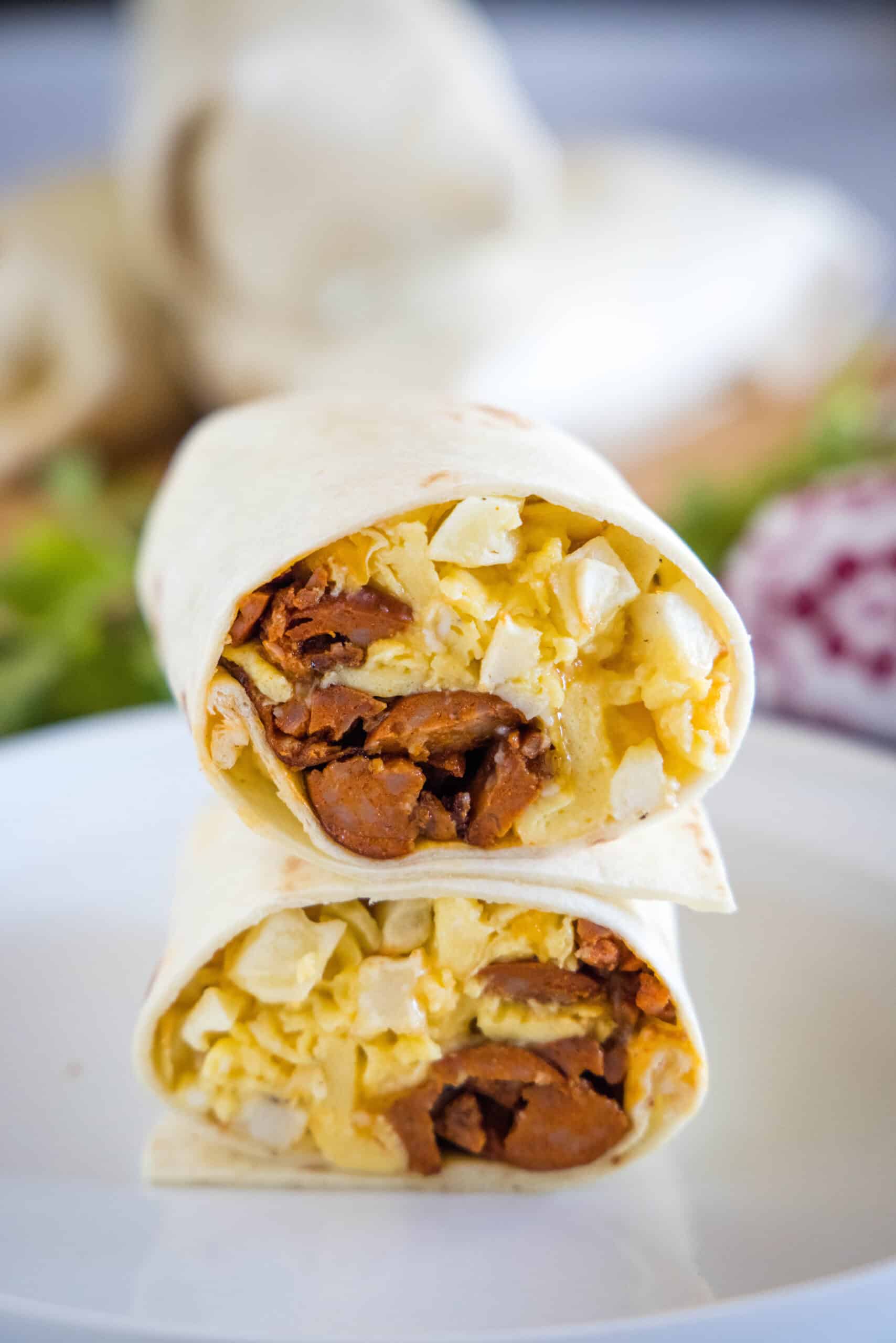 This chorizo breakfast burrito is a cheesy breakfast wrap loaded with crispy hash brown potatoes, spicy chorizo sausage, and fluffy eggs! Two halves of a chorizo breakfast burrito stacked on a plate, showing the eggs, cheese, potatoes, and chorizo filling inside.