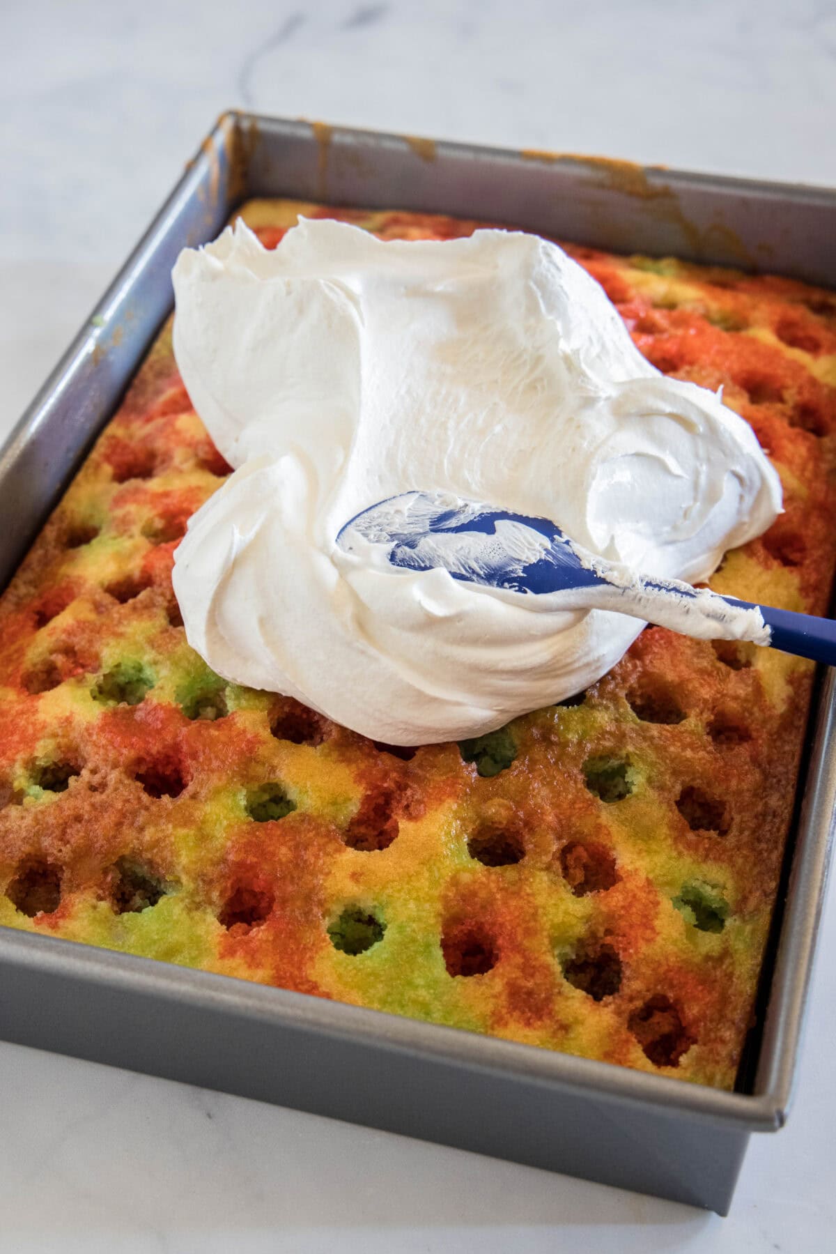 spreading whipped topping on poke cake