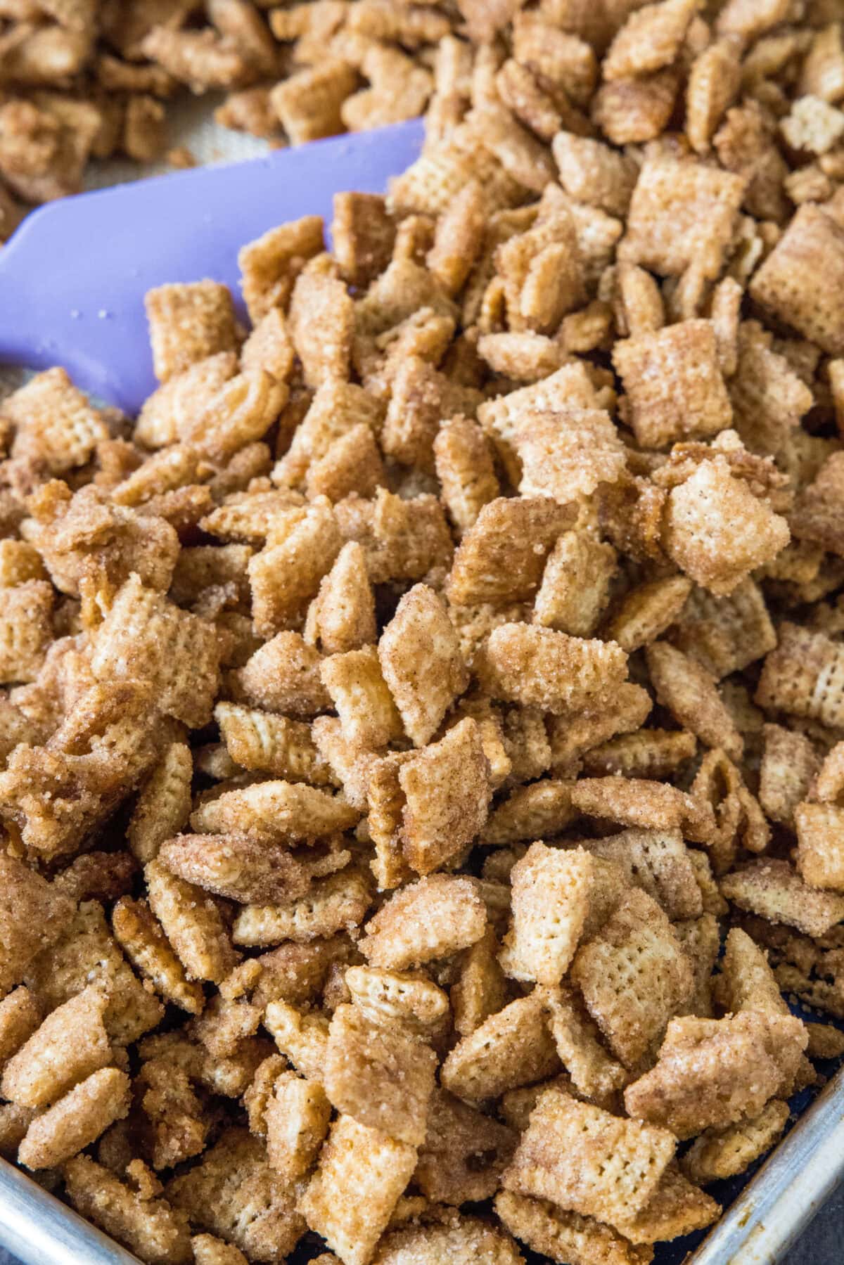 churro chex mix on a baking sheet stirring with a spatula
