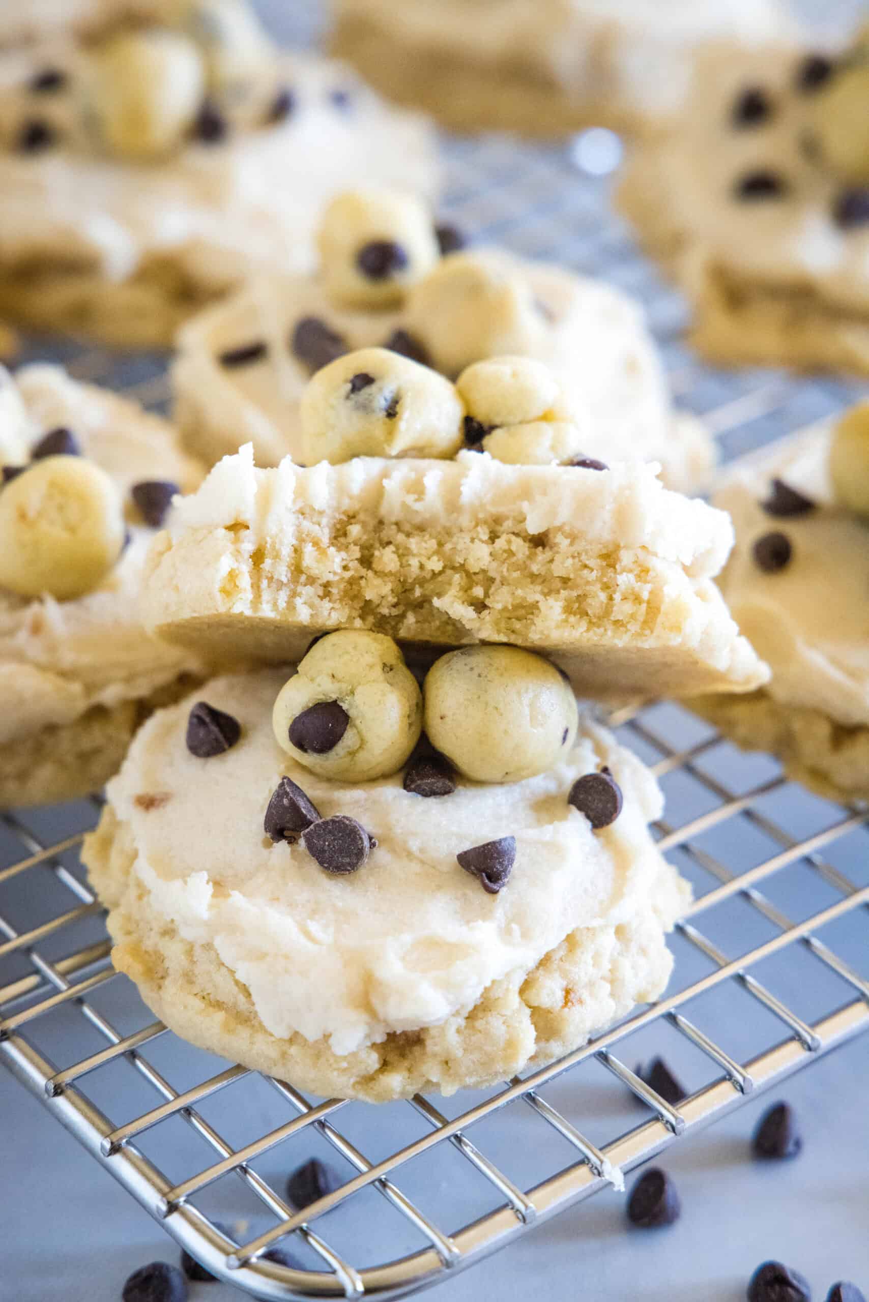 Frosted cookie dough cookies on a wire rack, with one cookie broken in half, propped up on another cookie.
