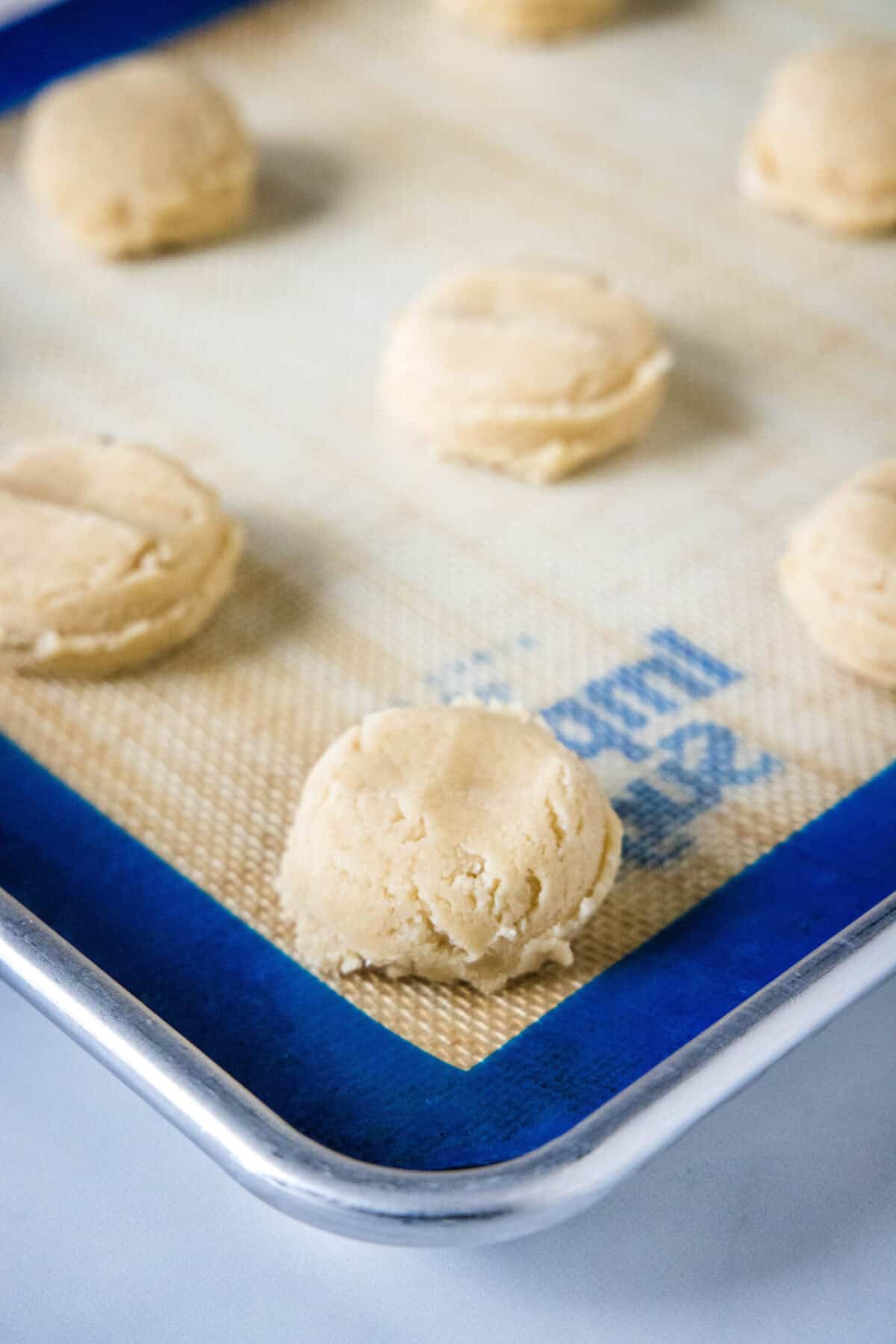 Cookie dough balls on a silpat-lined baking sheet.