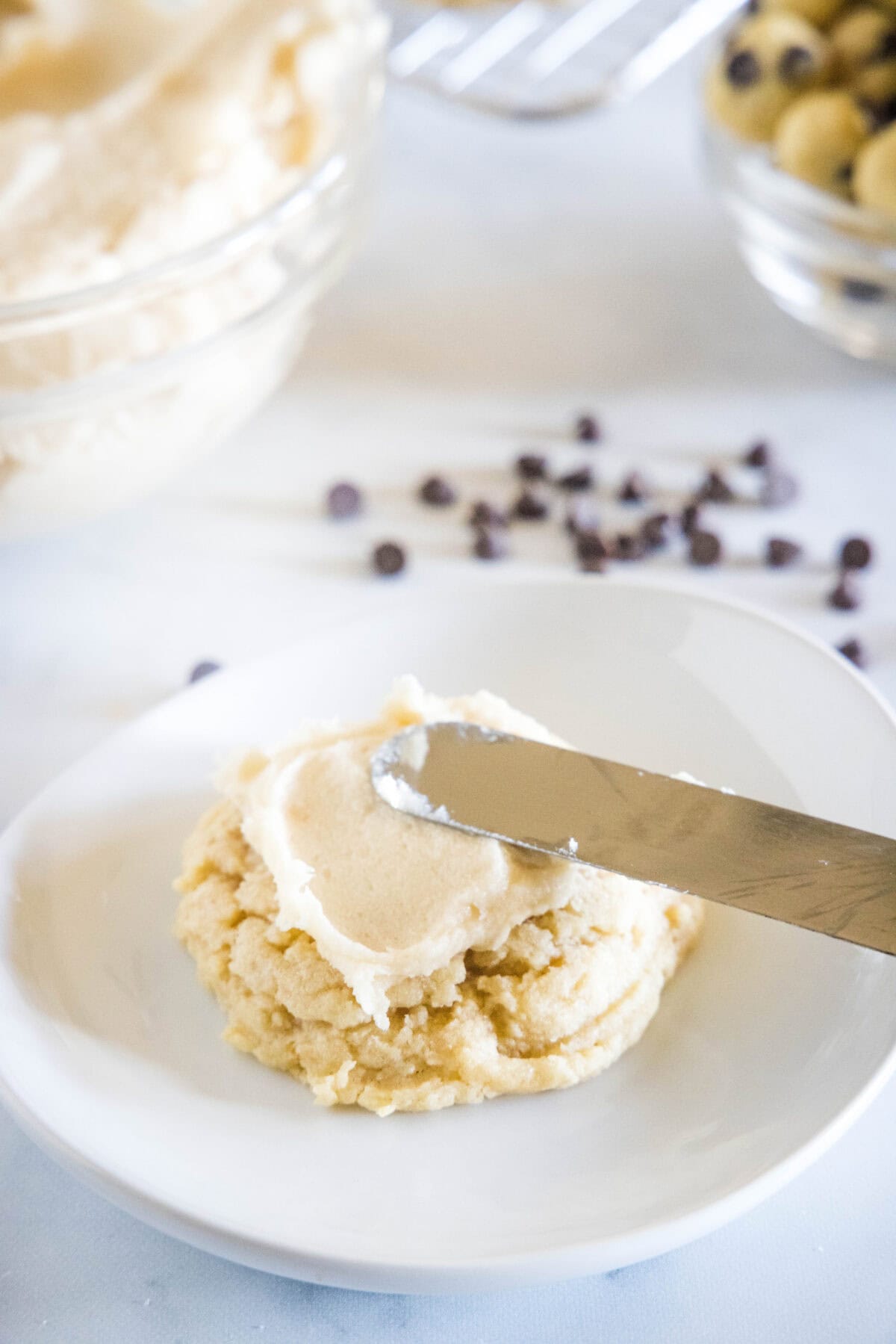 A knife spreading frosting over a cookie on a white plate.
