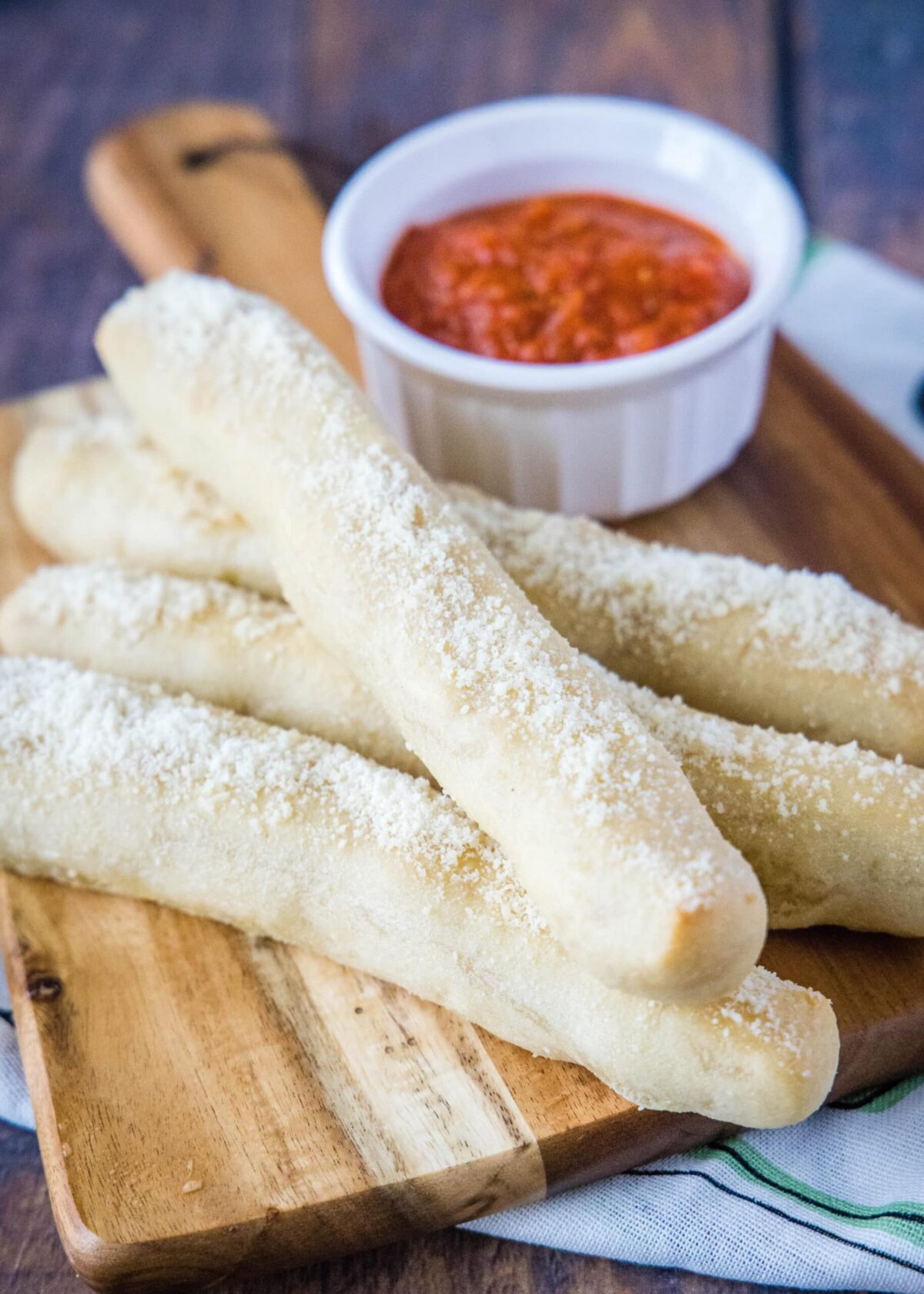 Four breadsticks on a cutting board in front of a ramekin of marinara sauce