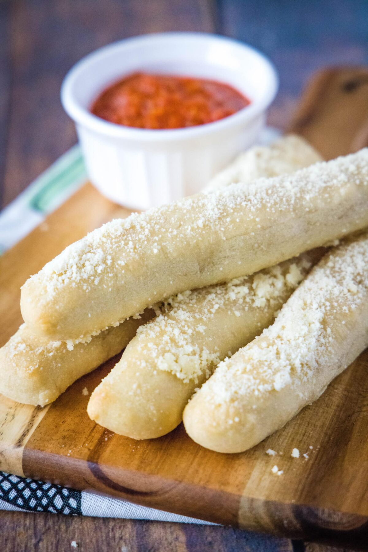 Four breadsticks on a cutting board with a ramekin of marinara in the background