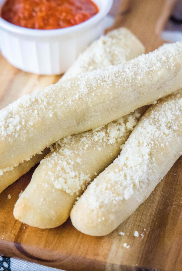 Four breadsticks on a cutting board with a ramekin of marinara sauce