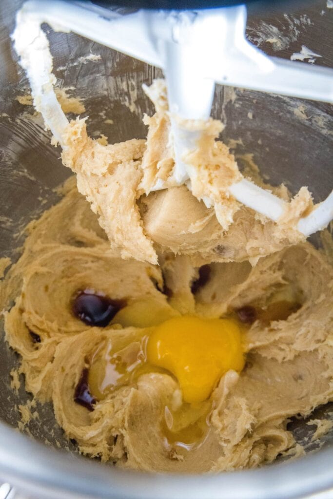 Wet cookie dough with an egg on top in a stand mixed bowl