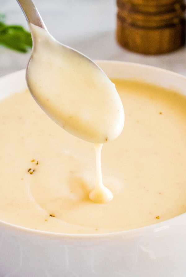 Close up of a spoonful of cream of chicken soup over a bowl of it, with parsley and salt and pepper grinders in the background.