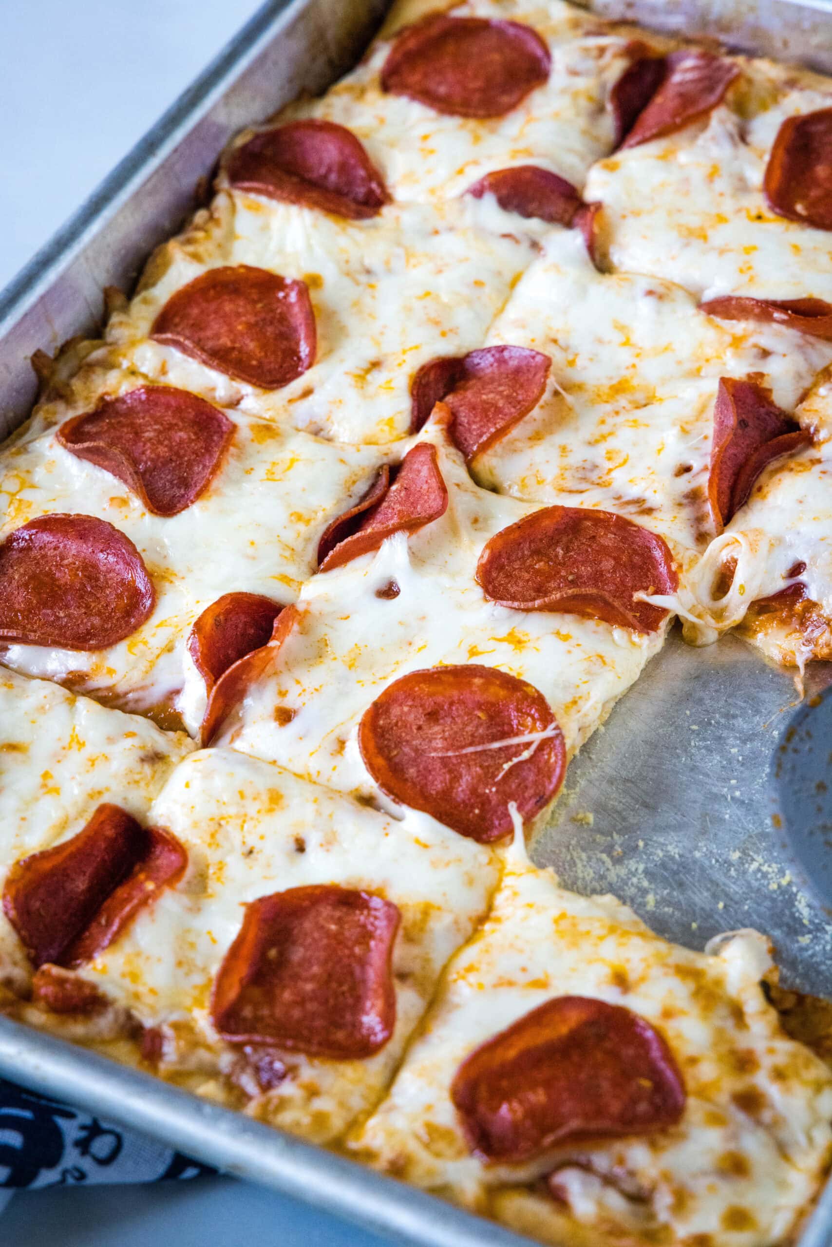 Pepperoni crescent roll pizza cut into squares on a baking sheet, with one slice missing.