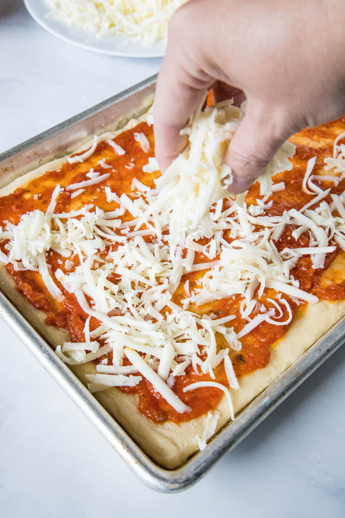 A hand sprinkling shredded mozzarella cheese over a crescent dough crust topped with pizza sauce.