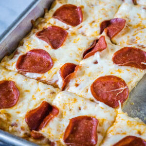 Pepperoni crescent roll pizza cut into squares on a baking sheet.