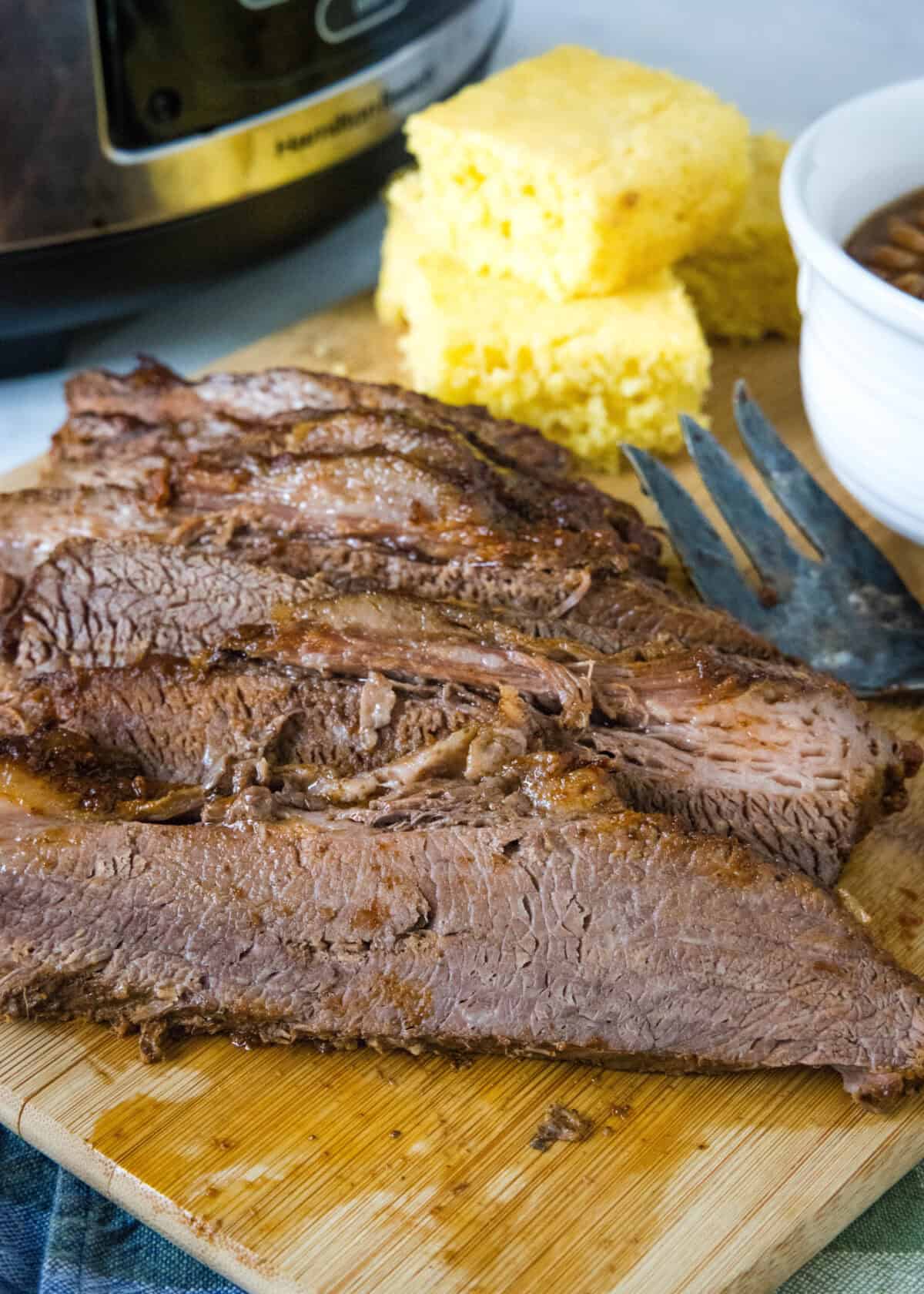 sliced brisket on cutting board with slow cooker in background