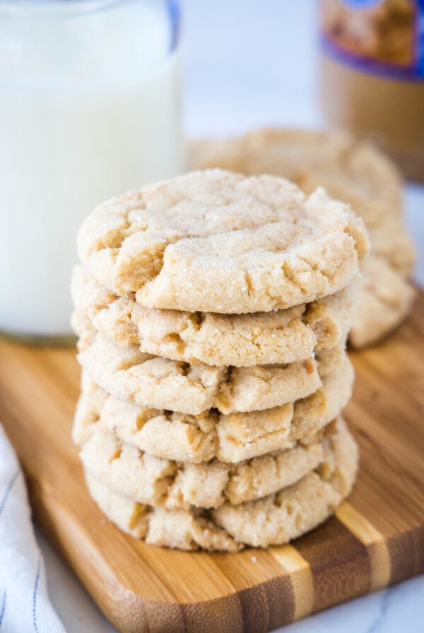 A stack of crunchy peanut butter cookies on a wooden cutting board.
