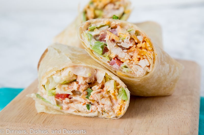 A chicken wrap cut in half diagonally, with one half resting on top of the other, with another wrap in the background