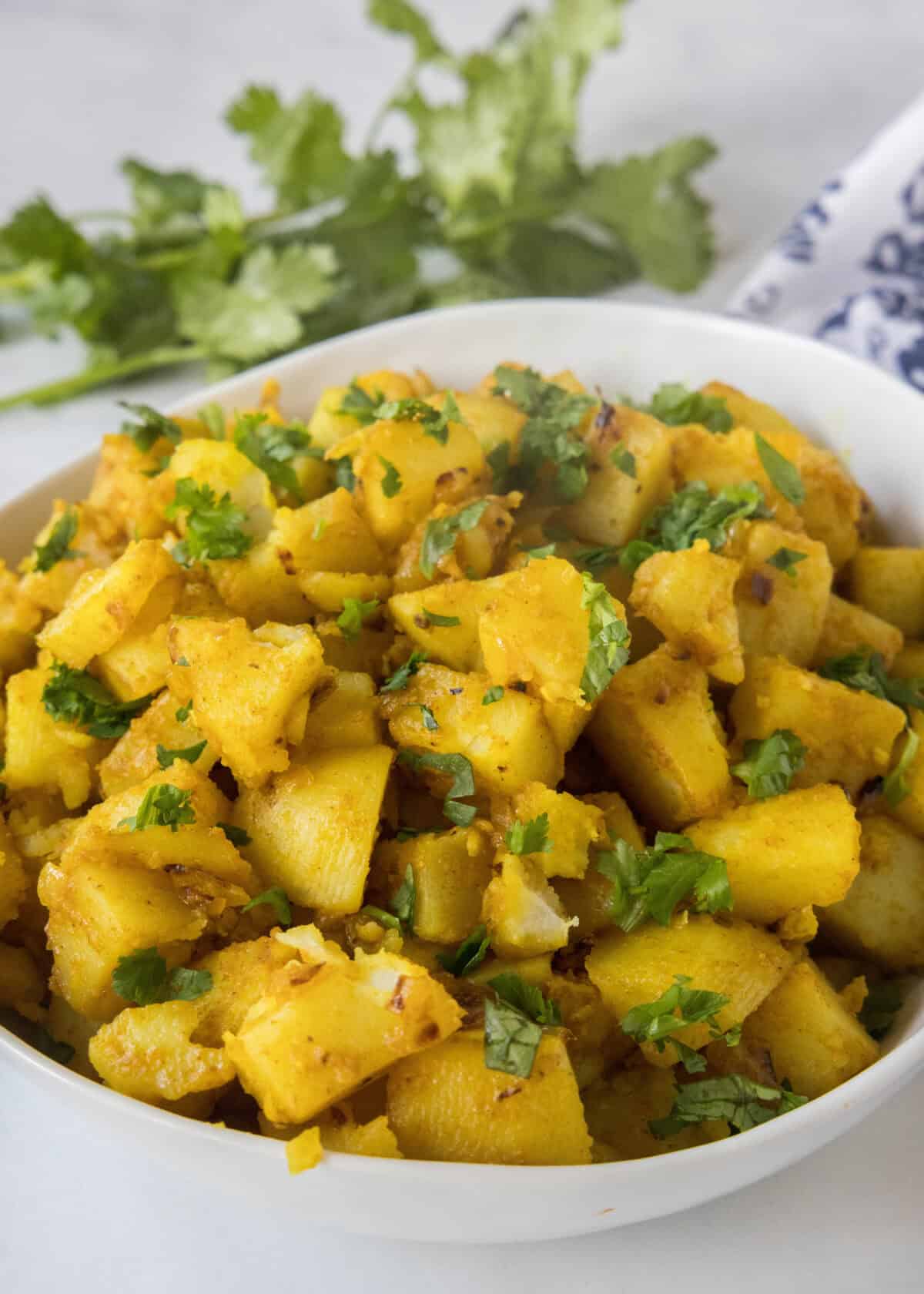 a serving bowl with curried potatoes topped with cilantro