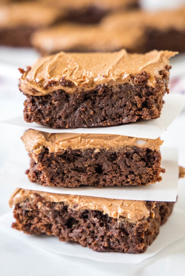 Three brownie squares with frosting stacked on top of each other.