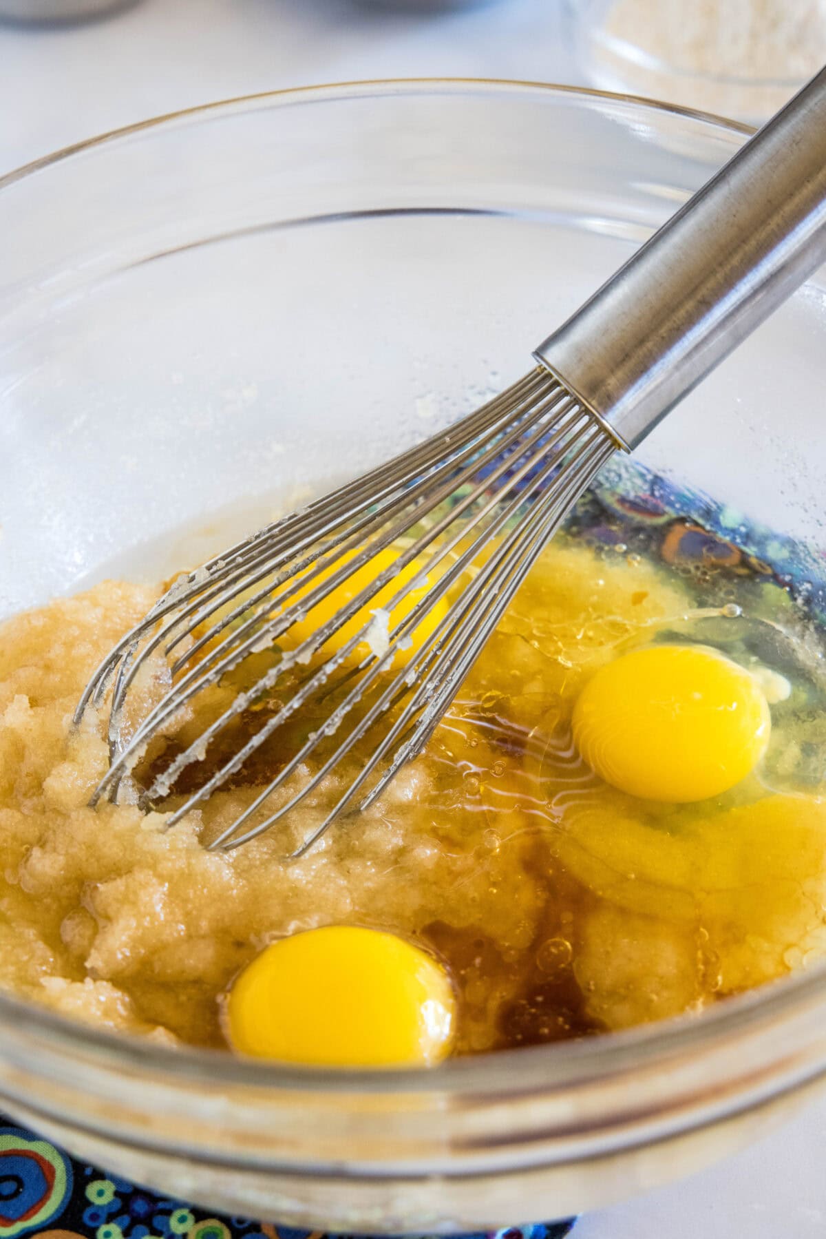 Eggs added to creamed sugar and butter in a glass mixing bowl with a whisk.