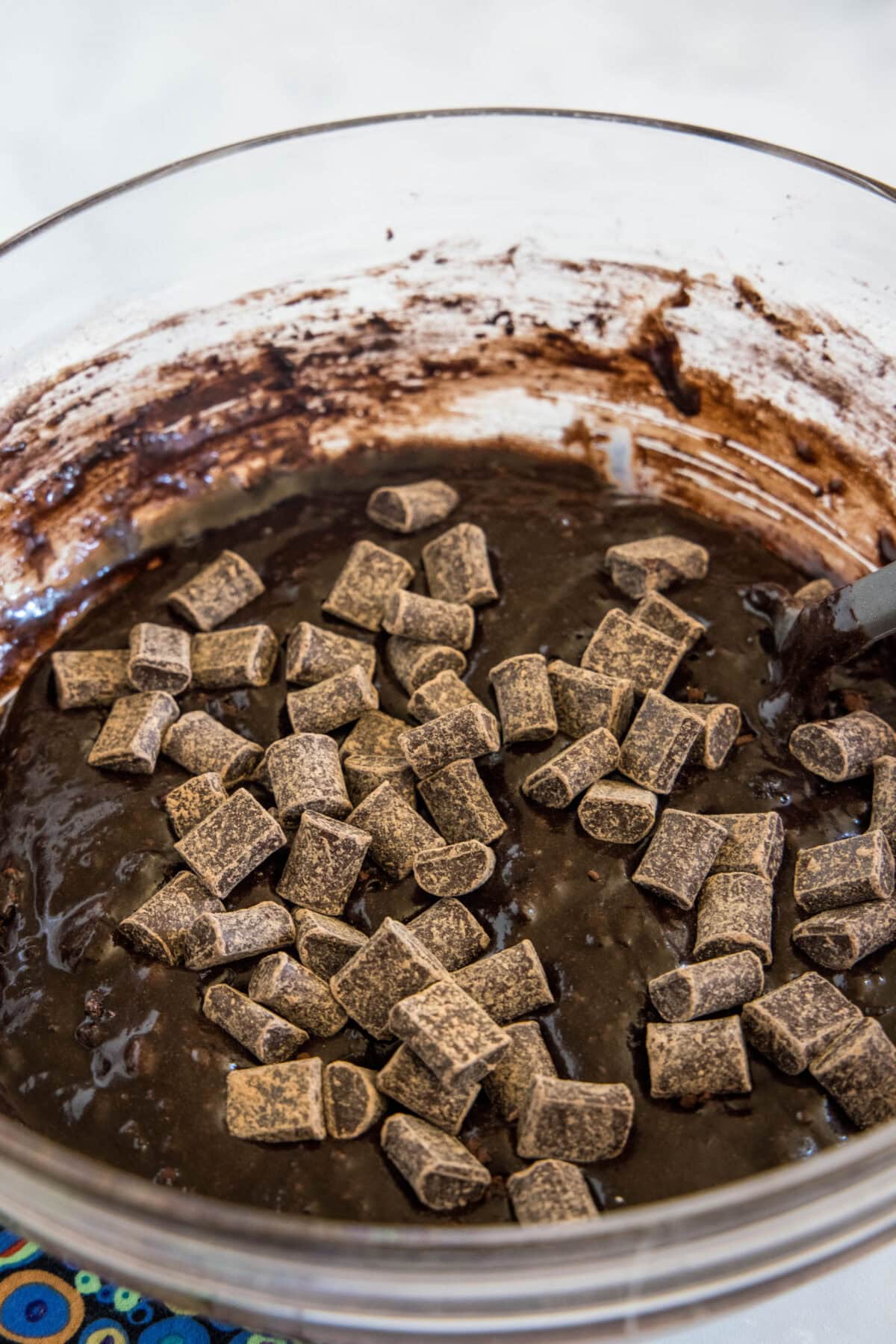 Chocolate chunks added to brownie batter in a glass mixing bowl.