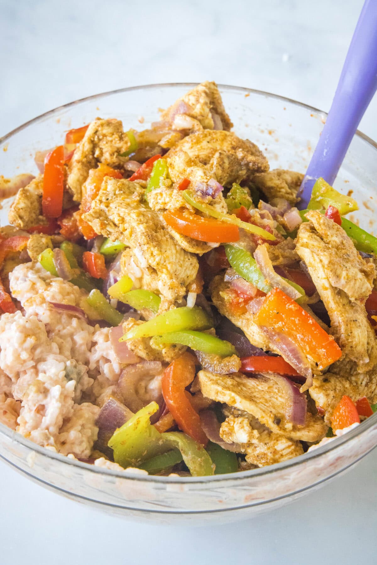 Chicken fajitas added to a sour cream, salsa, and rice mixture in a glass bowl.