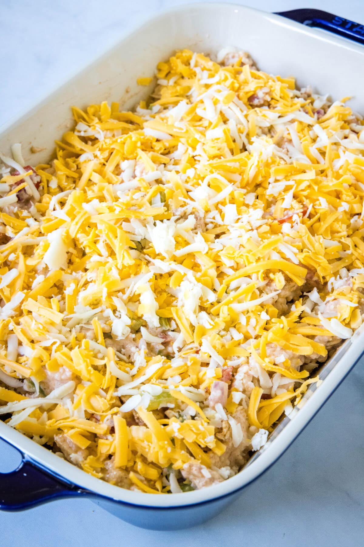 Unbaked chicken fajita casserole topped with shredded cheese in a baking dish.