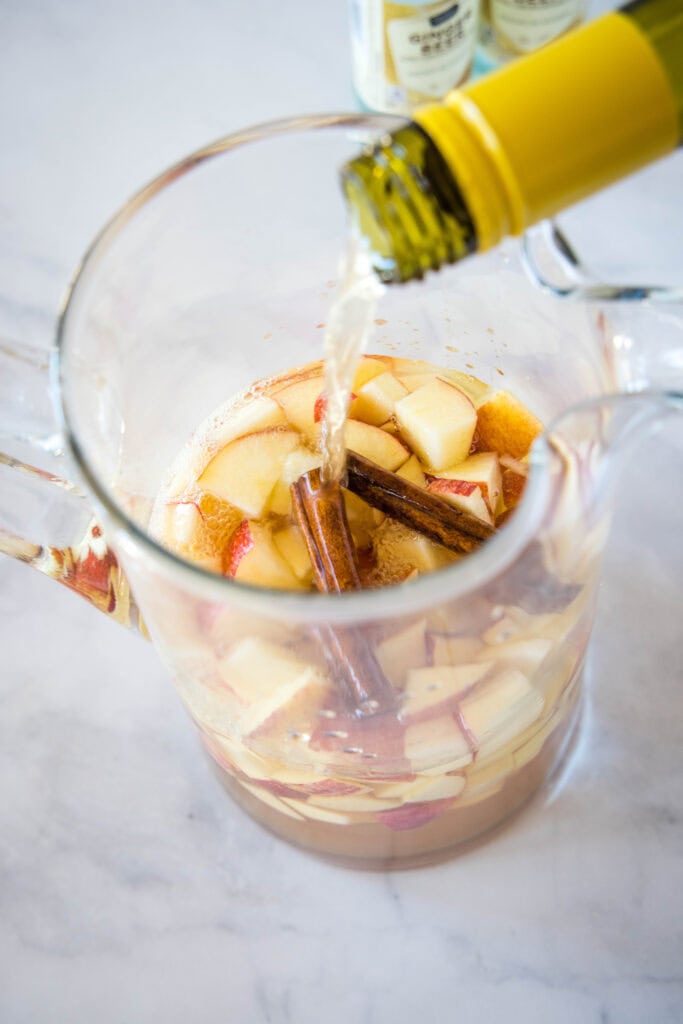 pouring white wine into a pitcher over chopped apples
