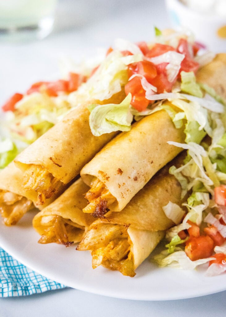 chicken flautas on a white plate with lettuce and tomatoes on top