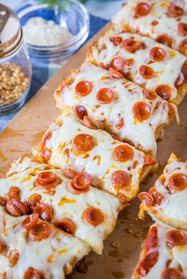 French bread pizza cut into slices on a wooden cutting board.