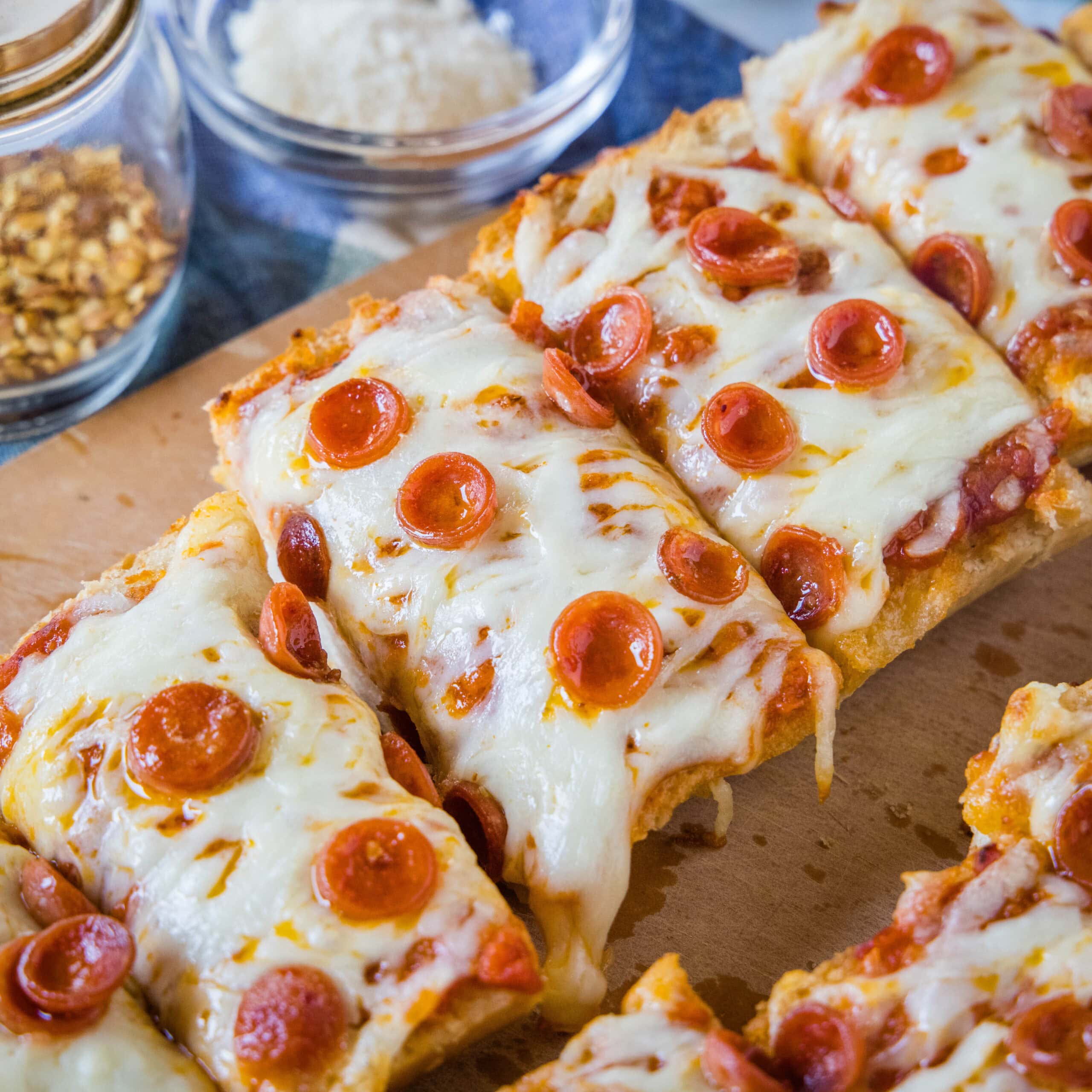 French bread pizza cut into slices on a wooden cutting board.