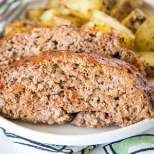 Onion soup meatloaf slices on a plate with roasted potatoes in the background.