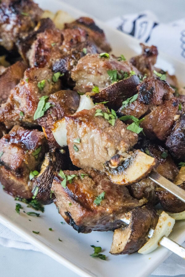 A stack of beef, mushroom, and onion kabobs on a plate