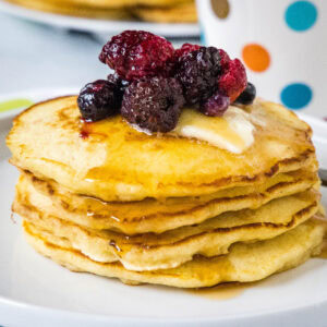 A stack of griddle cakes topped with mixed berries and syrup on a white plate.