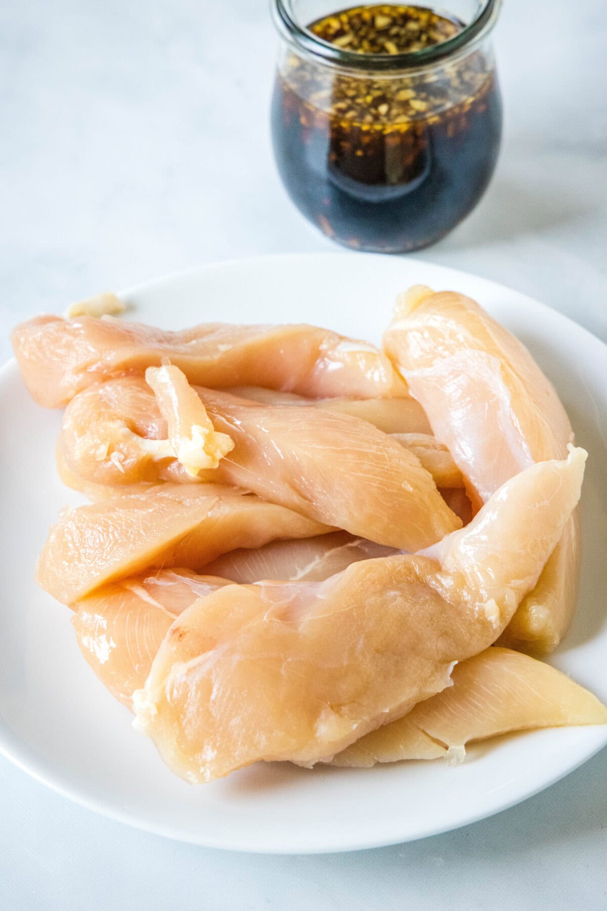 Chicken pieces on a white plate with a jar of teriyaki sauce in the background.