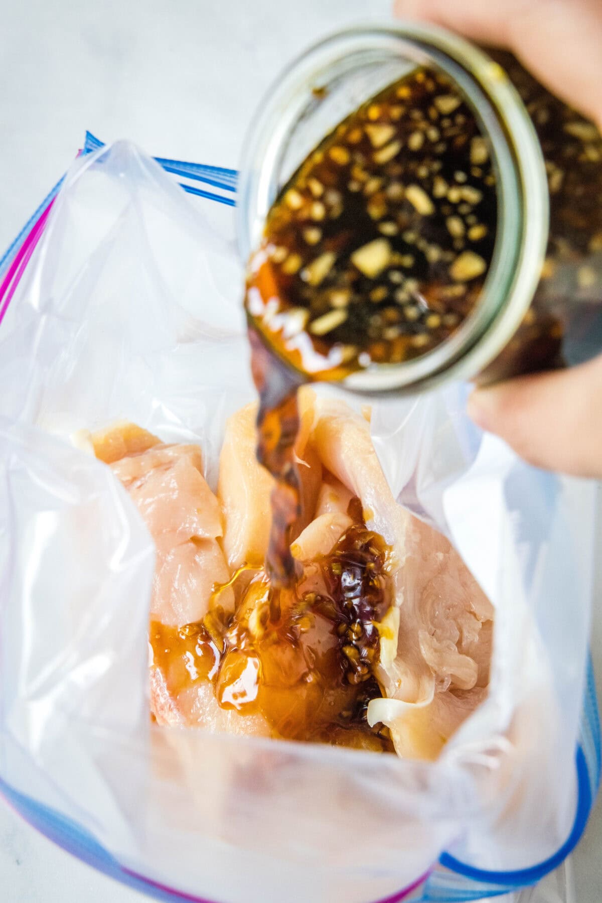 Pouring homemade teriyaki marinade into a bag with chicken pieces.