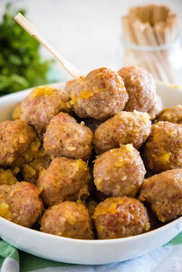 Ham balls with pineapple sauce piled into a bowl with a jar of cocktail skewers in the background.