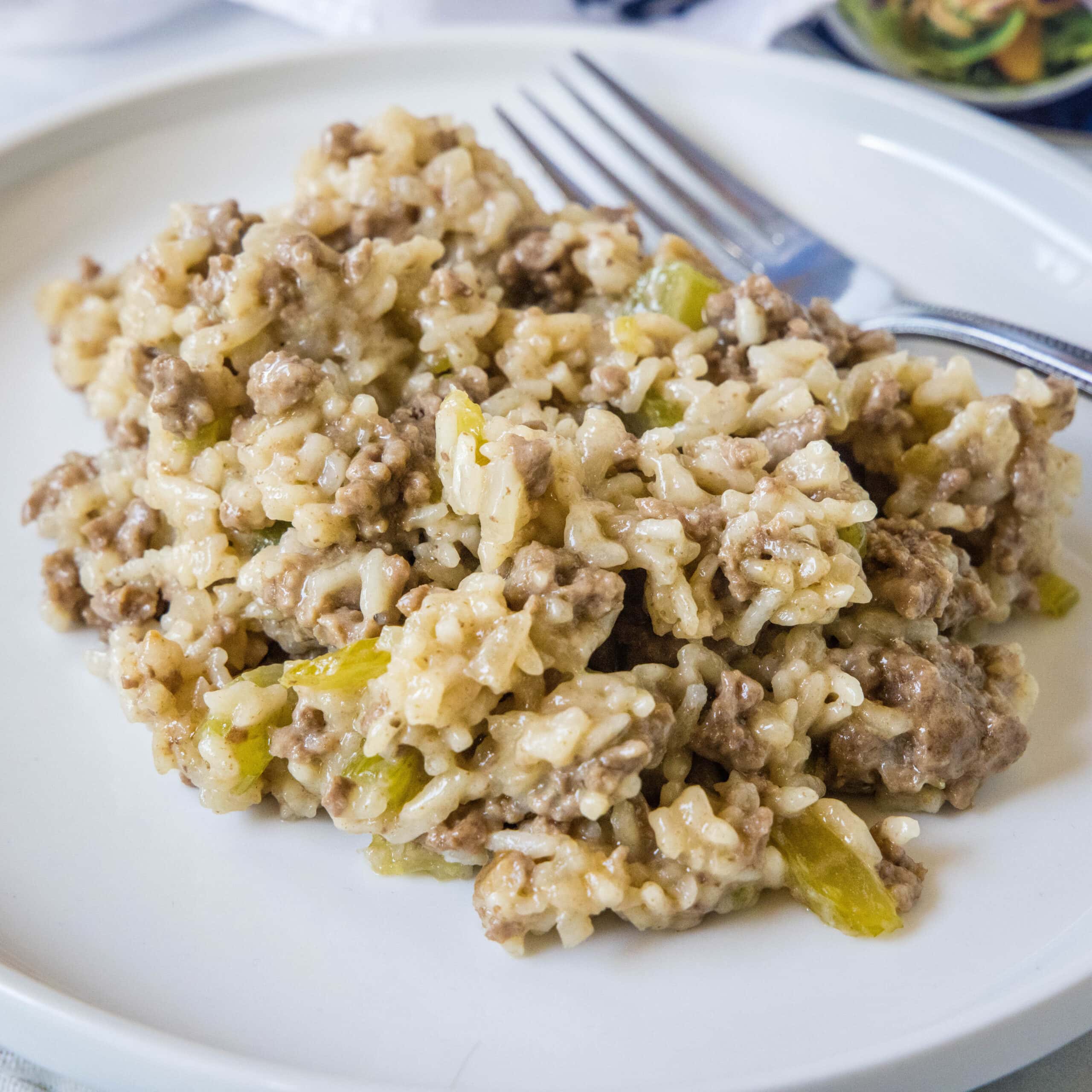 A serving of hamburger rice casserole next to a fork on a white plate.