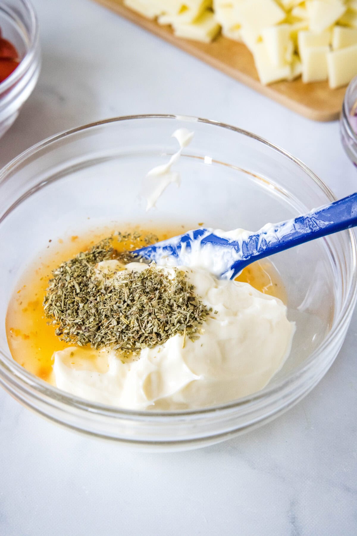 Dressing ingredients added to a glass bowl with a blue spatula for stirring.
