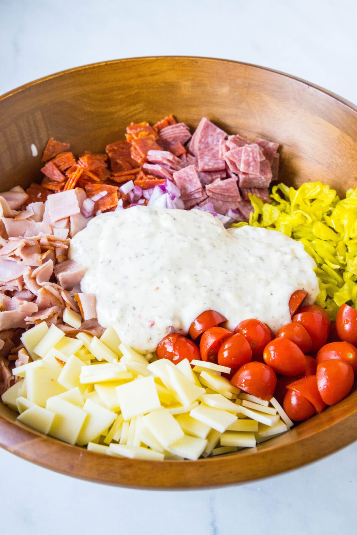 Dressing added to hoagie dip ingredients in a wooden salad bowl.