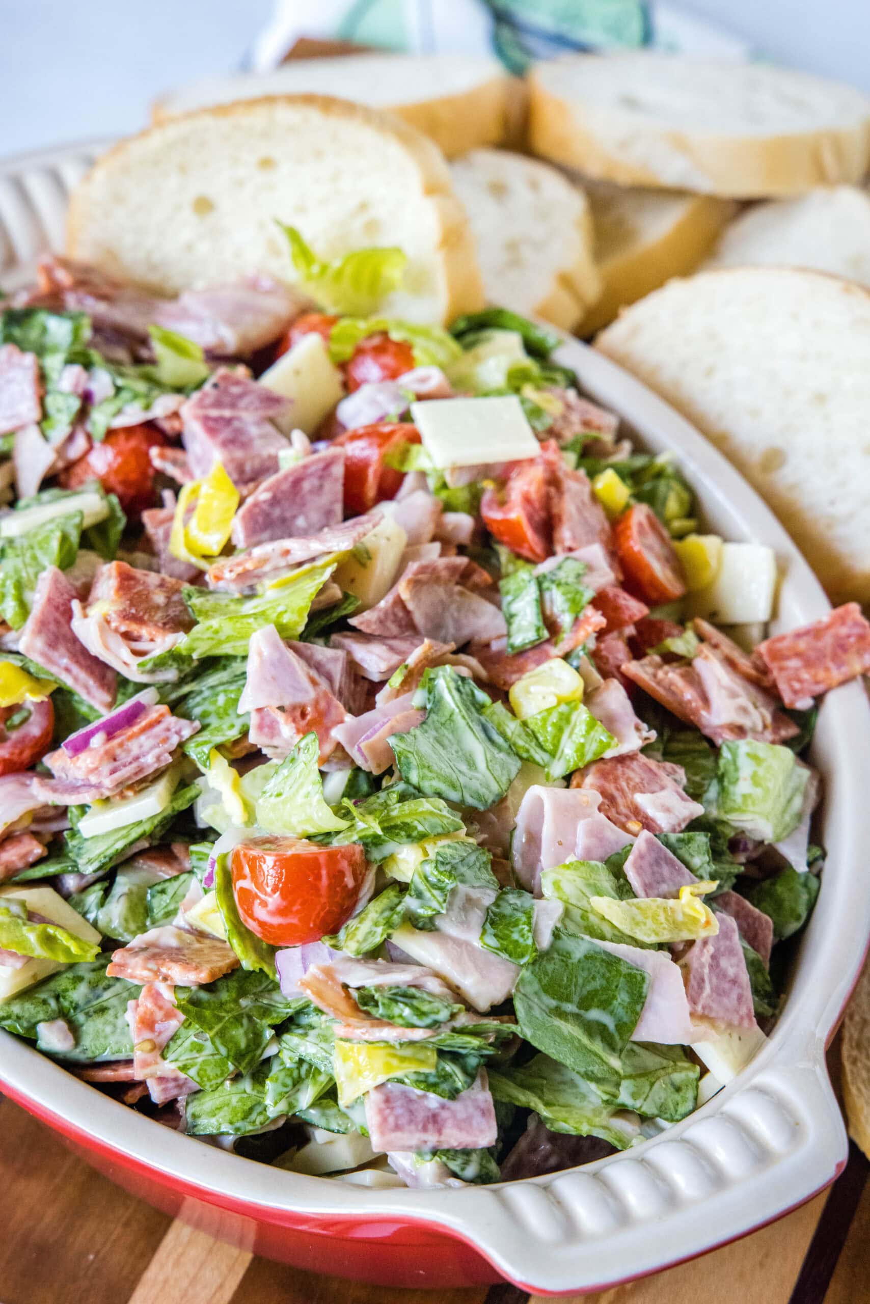 This fresh and zesty hoagie dip has all the flavors of an Italian sub sandwich! Serve this dip as an easy appetizer spread over crusty bread. Hoagie dip in a red ceramic serving bowl with bread slices in the background.