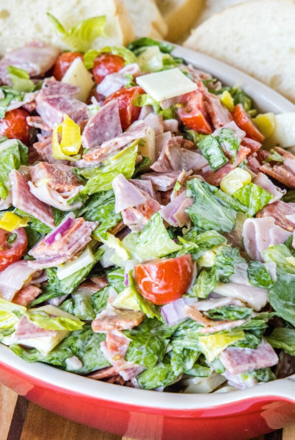 Hoagie dip in a red ceramic serving bowl with bread slices in the background.