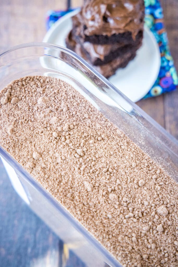 container of brownie mix with plate of brownies in the background