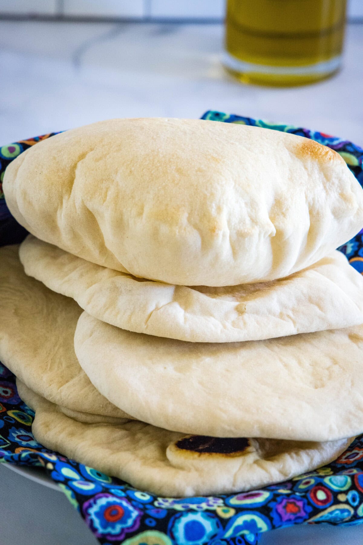 Fluffy homemade pita breads stacked on a blue cloth.