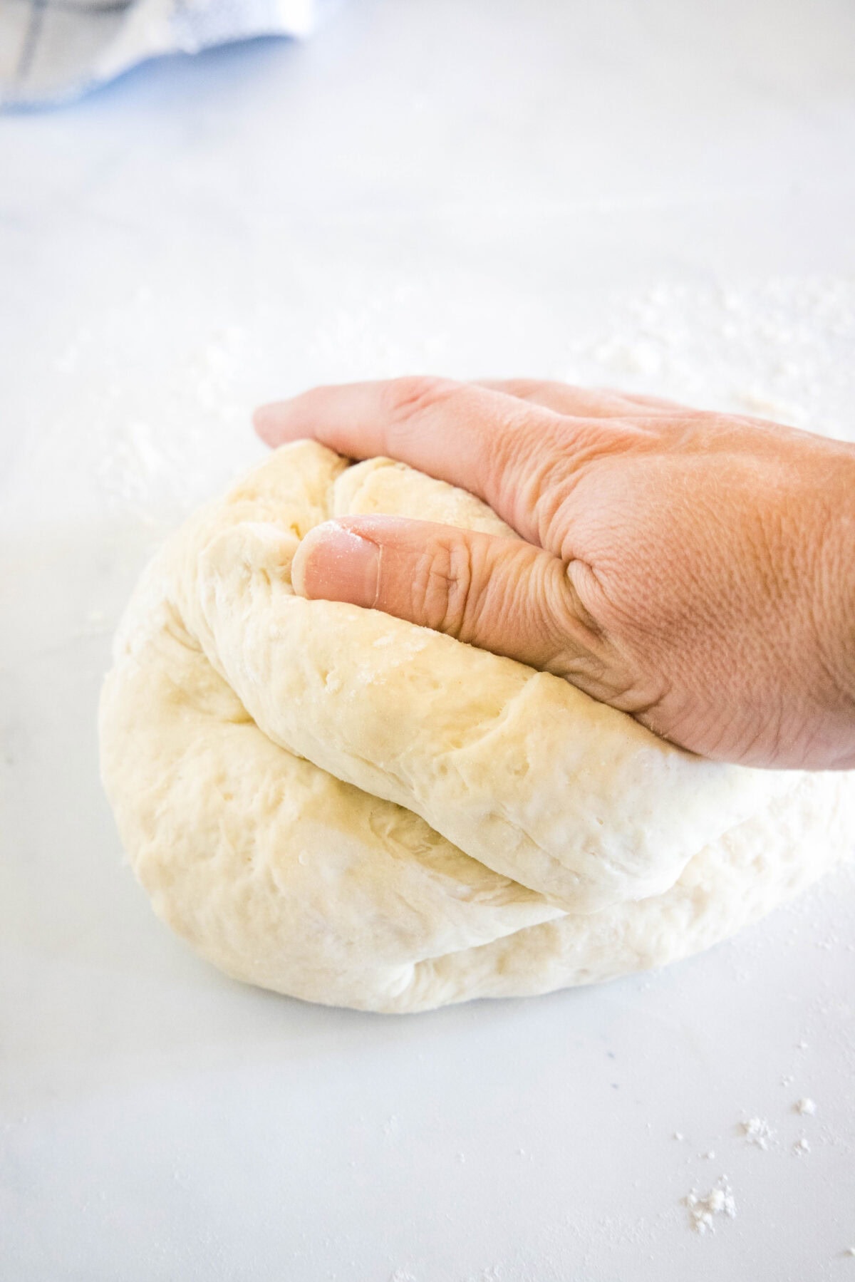 A hand kneading pita dough on a white surface.