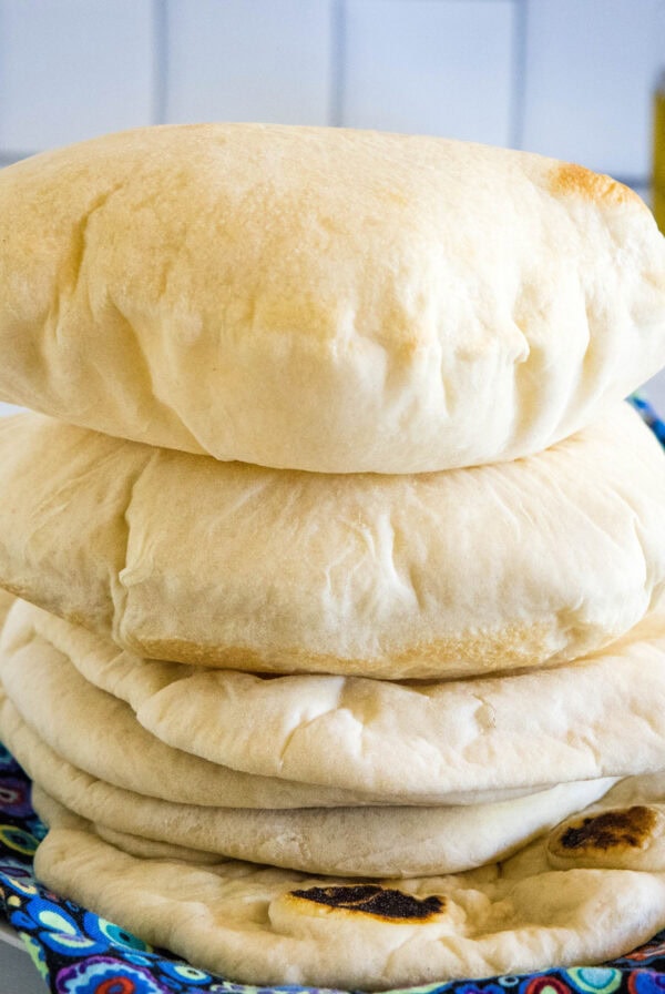 Fluffy homemade pita breads stacked on a blue cloth.