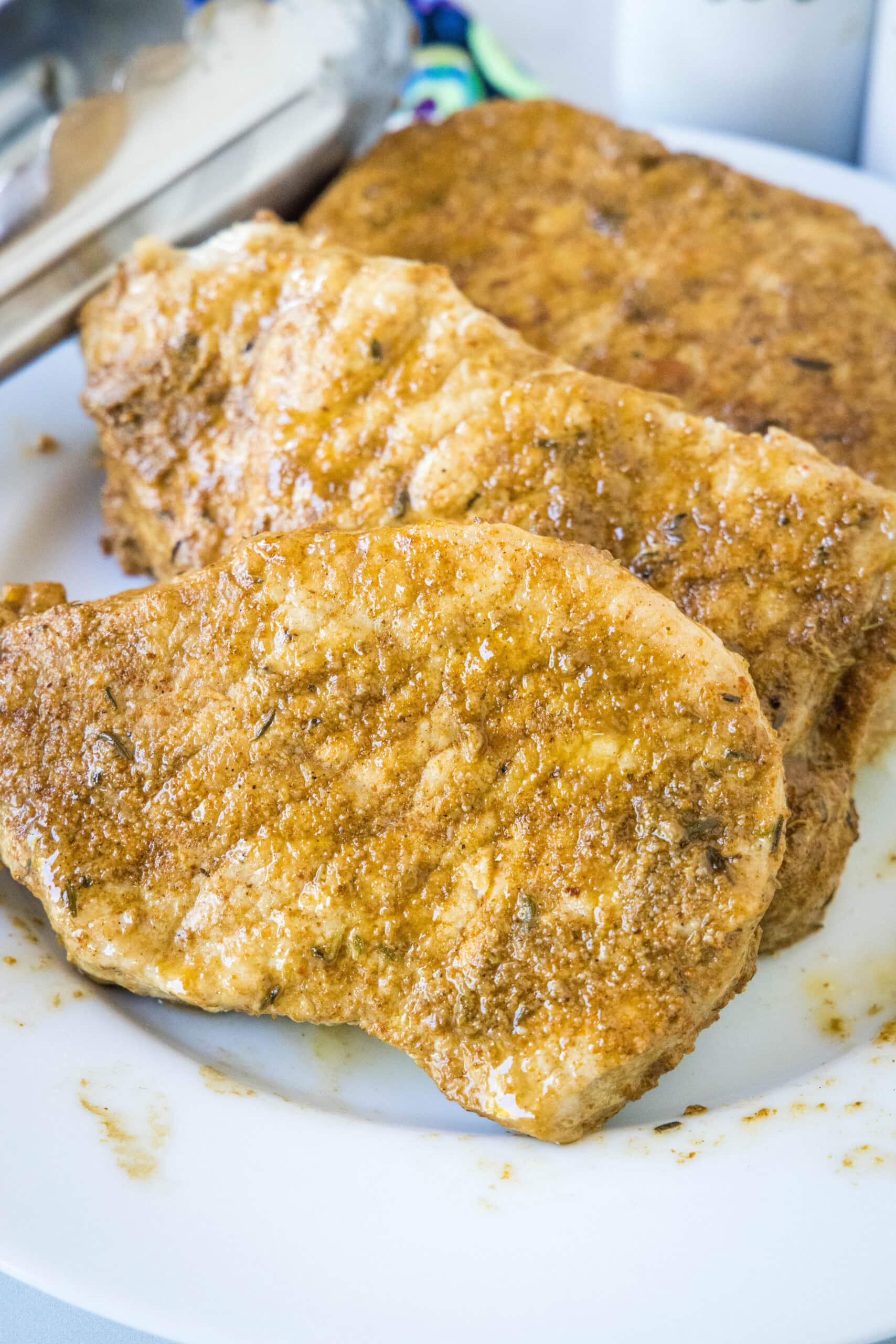 Cooked seasoned pork chops on a white plate next to a set of tongs.