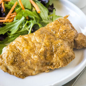 An instant pot pork chop with a side of salad on a white plate.