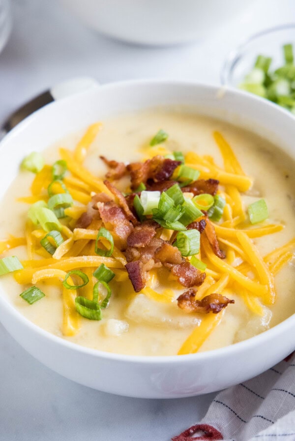 Close up of a bowl of potato soup with cheese, bacon, and green onions on top.
