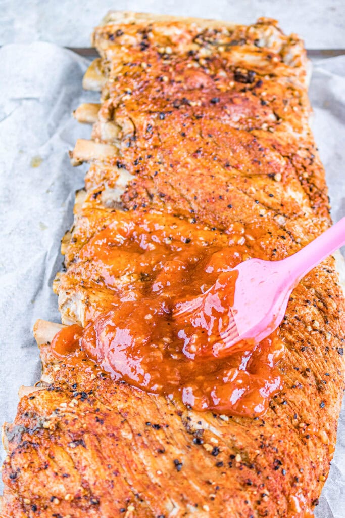 cooked ribs being brushed with barbecue sauce